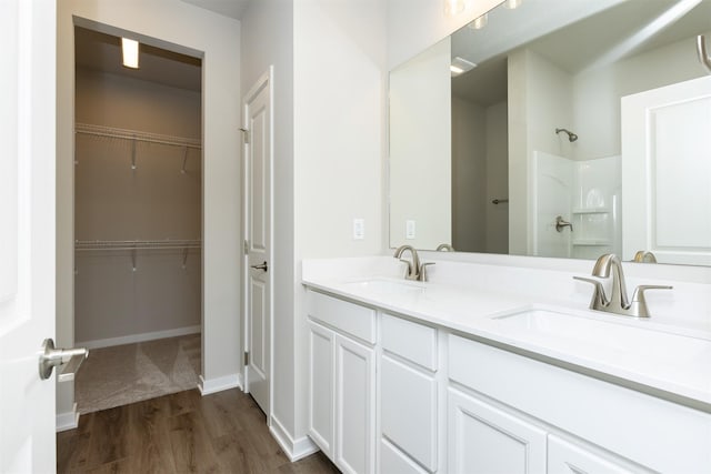 full bathroom with a spacious closet, wood finished floors, a sink, and a shower