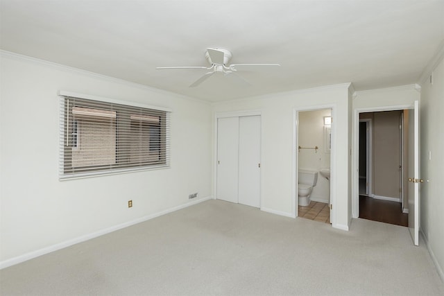 unfurnished bedroom with ceiling fan, ensuite bath, crown molding, light carpet, and a closet