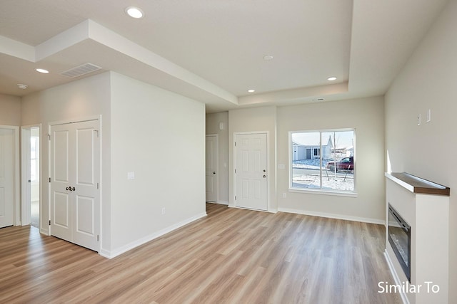 unfurnished living room with light wood-style flooring, visible vents, a raised ceiling, and recessed lighting