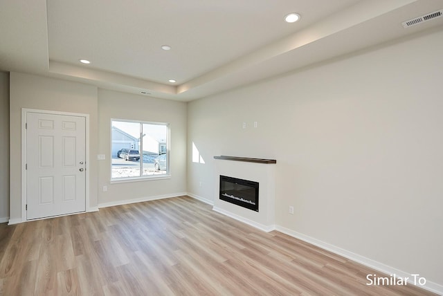 unfurnished living room with light wood-type flooring and a tray ceiling