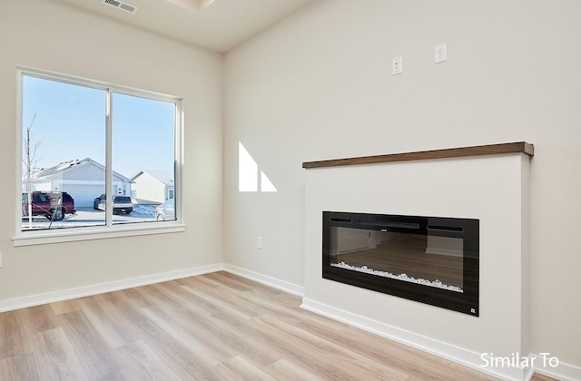 unfurnished living room featuring light wood-type flooring, visible vents, baseboards, and a glass covered fireplace