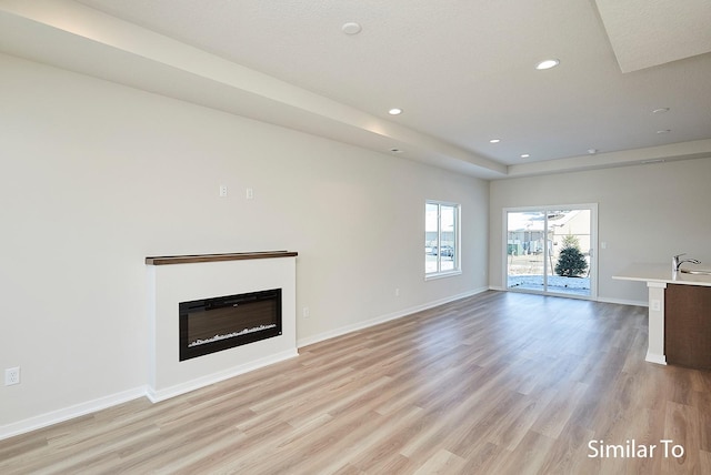 unfurnished living room featuring light wood-style flooring, baseboards, and a glass covered fireplace