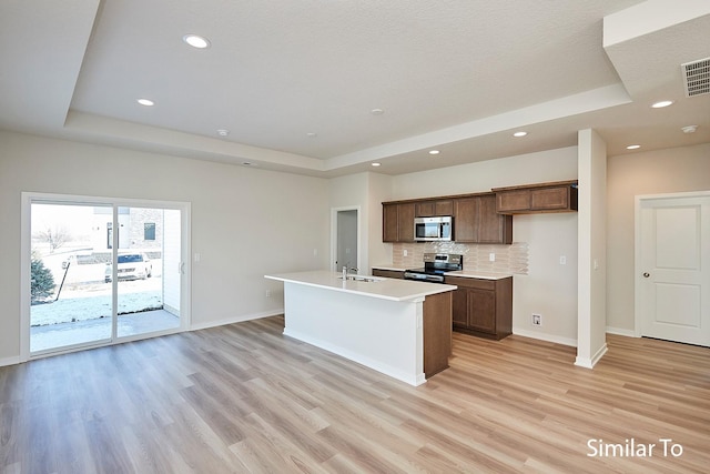 kitchen featuring stainless steel appliances, a raised ceiling, a center island with sink, and light hardwood / wood-style floors