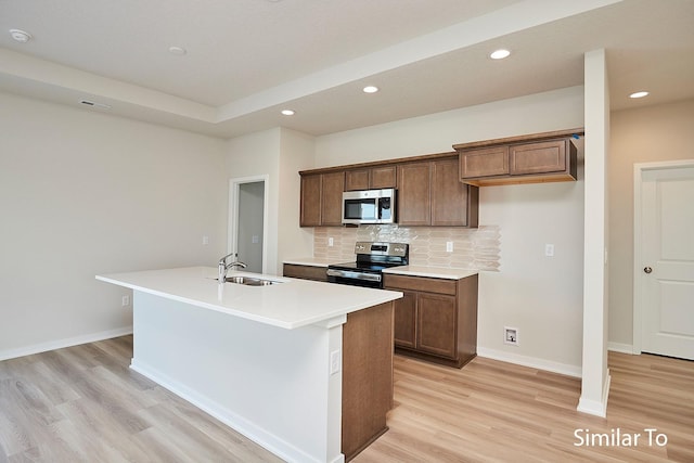 kitchen with a kitchen island with sink, sink, light wood-type flooring, appliances with stainless steel finishes, and tasteful backsplash