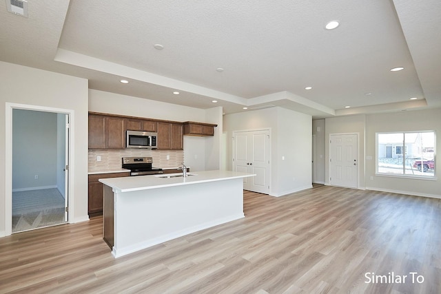 kitchen with appliances with stainless steel finishes, sink, a tray ceiling, and an island with sink