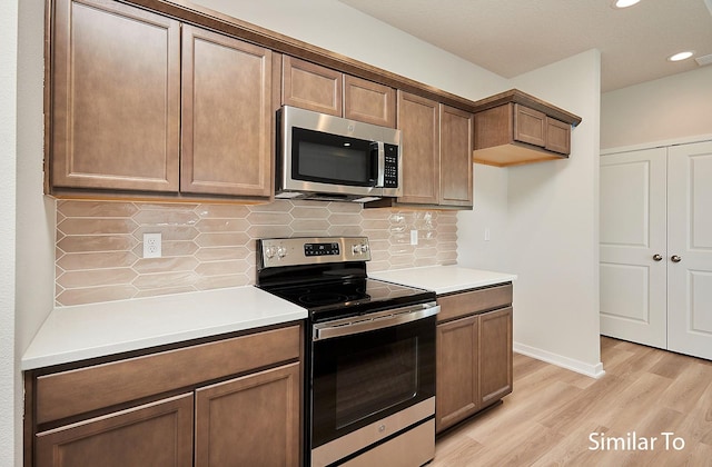 kitchen featuring light wood finished floors, tasteful backsplash, stainless steel appliances, and light countertops