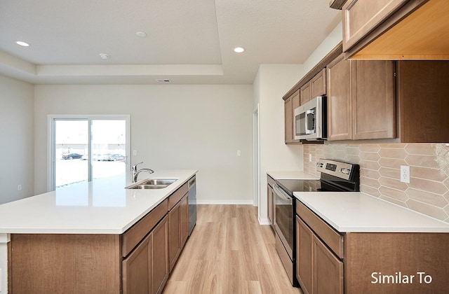 kitchen featuring sink, stainless steel appliances, backsplash, a center island with sink, and light wood-type flooring