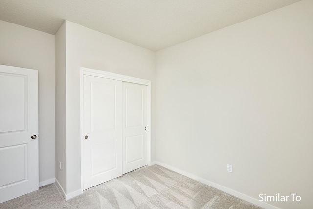 unfurnished bedroom with a closet, light carpet, and baseboards