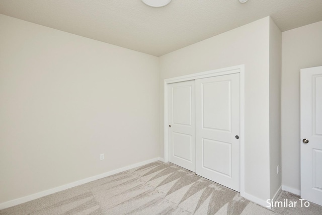 unfurnished bedroom with baseboards, a closet, a textured ceiling, and light colored carpet