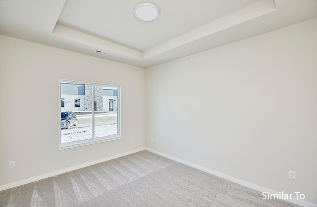 carpeted spare room featuring a tray ceiling, visible vents, and baseboards