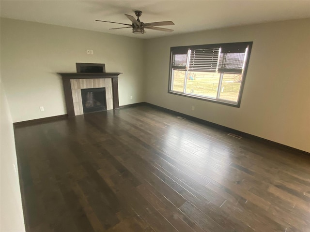 unfurnished living room with ceiling fan, dark wood-type flooring, and a tile fireplace