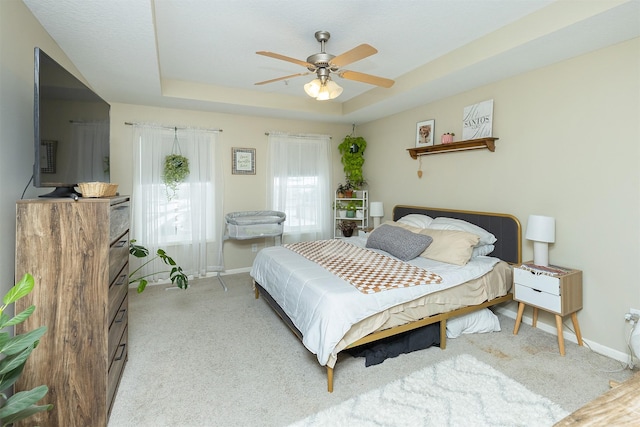 bedroom featuring light carpet, a tray ceiling, and ceiling fan