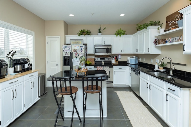 kitchen featuring sink, dark tile patterned floors, appliances with stainless steel finishes, white cabinetry, and a breakfast bar area