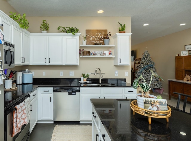 kitchen with appliances with stainless steel finishes, dark stone counters, a textured ceiling, sink, and white cabinetry