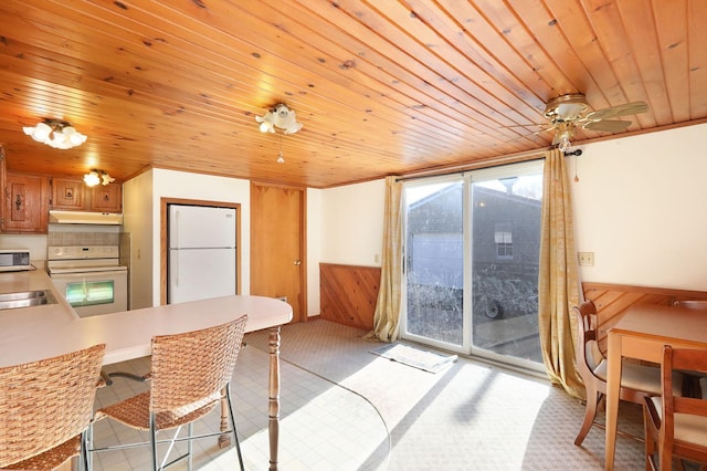 dining area featuring a ceiling fan, wood ceiling, a wainscoted wall, and wooden walls