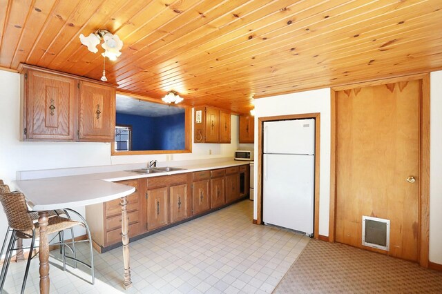 kitchen with white appliances, a kitchen bar, sink, and wooden ceiling