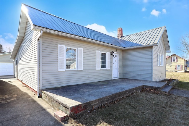 back of house featuring a garage, a patio, a chimney, metal roof, and an outbuilding