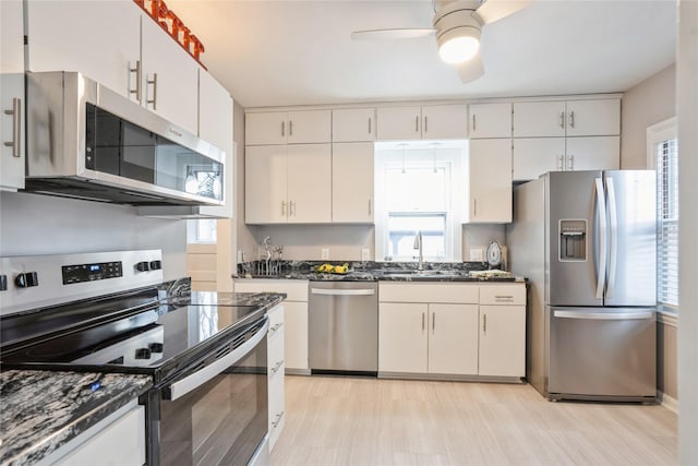 kitchen with stainless steel appliances, sink, dark stone countertops, white cabinetry, and plenty of natural light