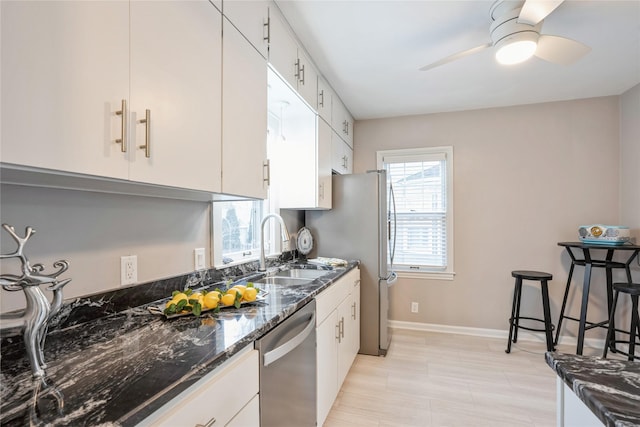 kitchen featuring dark stone counters, sink, stainless steel dishwasher, ceiling fan, and white cabinetry