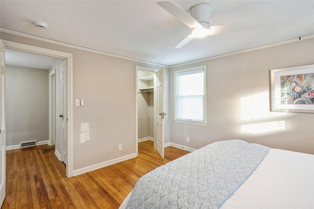 bedroom with hardwood / wood-style floors, a walk in closet, ceiling fan, and crown molding