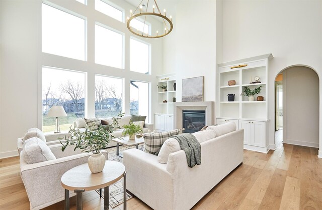 living room featuring a towering ceiling, built in shelves, light wood-type flooring, and a chandelier