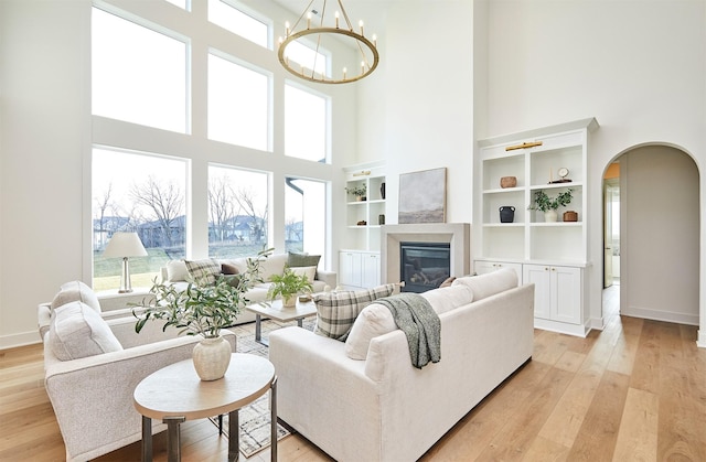 living room featuring an inviting chandelier, a towering ceiling, built in features, and light wood-type flooring