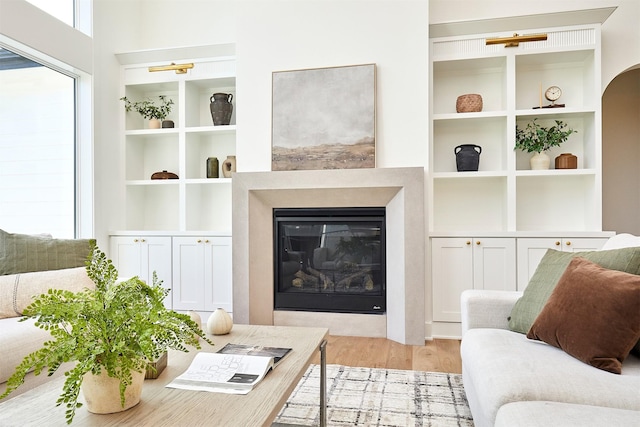 living room with built in shelves, arched walkways, wood finished floors, and a glass covered fireplace