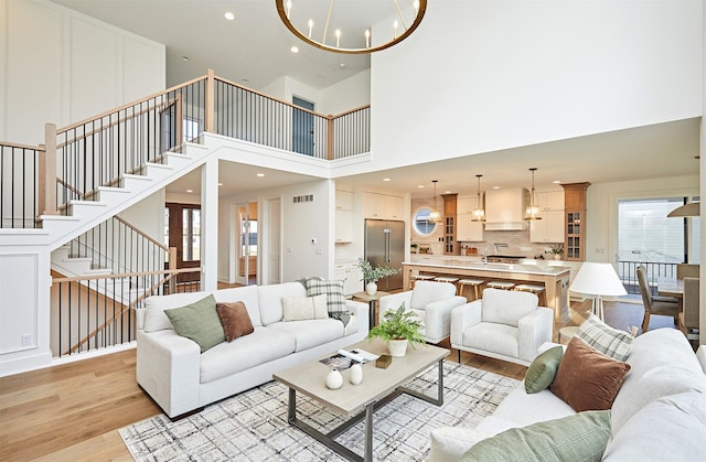 living area with light wood-style flooring, a notable chandelier, visible vents, a healthy amount of sunlight, and stairs