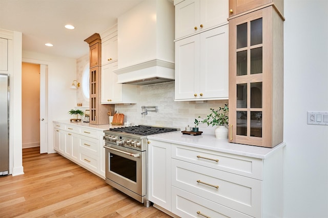 kitchen featuring tasteful backsplash, light wood-style flooring, custom range hood, glass insert cabinets, and stainless steel appliances