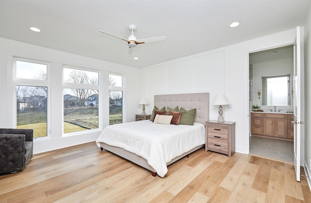 bedroom with recessed lighting, a decorative wall, light wood-style flooring, a sink, and ensuite bath