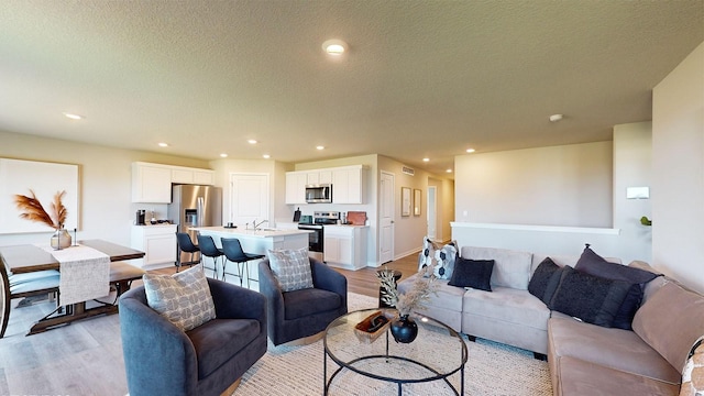 living room with a textured ceiling, light hardwood / wood-style flooring, and sink