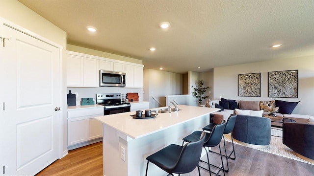 kitchen with a center island with sink, appliances with stainless steel finishes, light hardwood / wood-style floors, a kitchen bar, and white cabinetry