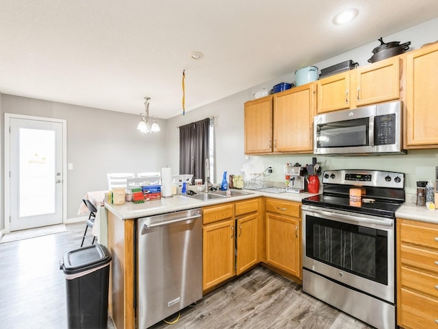 kitchen featuring sink, stainless steel appliances, a notable chandelier, kitchen peninsula, and light wood-type flooring