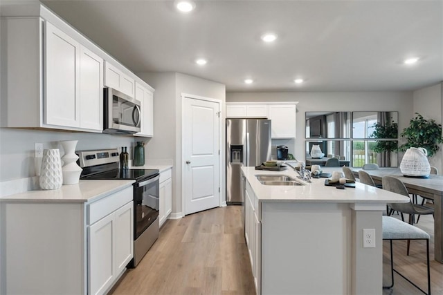 kitchen featuring appliances with stainless steel finishes, sink, white cabinets, a kitchen island with sink, and light hardwood / wood-style flooring