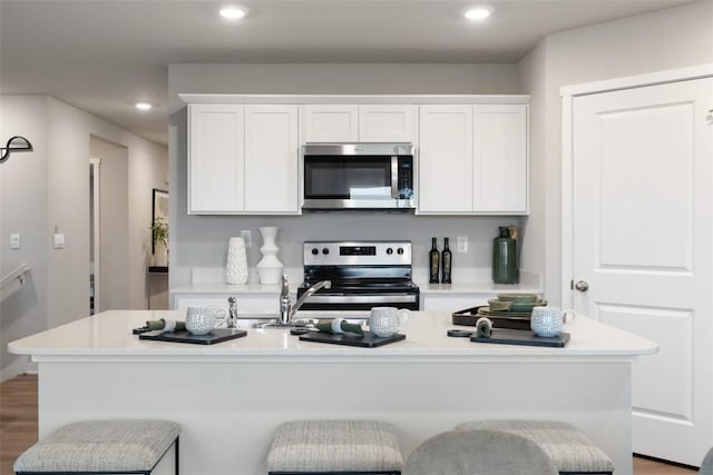 kitchen with white cabinetry, appliances with stainless steel finishes, a kitchen island with sink, and a kitchen breakfast bar