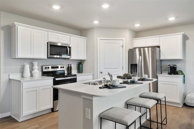 kitchen with white cabinetry, an island with sink, sink, stainless steel appliances, and light wood-type flooring