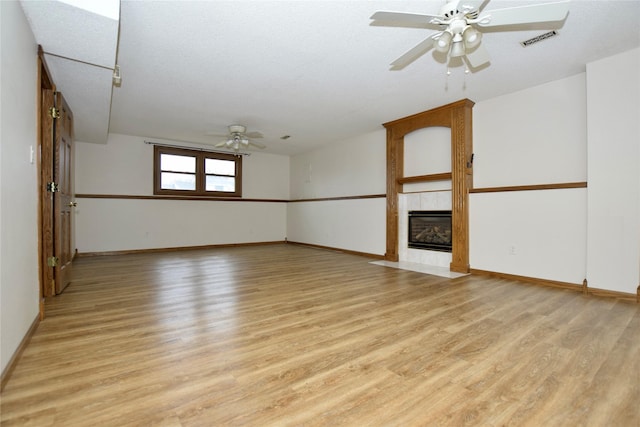 empty room featuring a textured ceiling, light hardwood / wood-style floors, ceiling fan, and a tiled fireplace