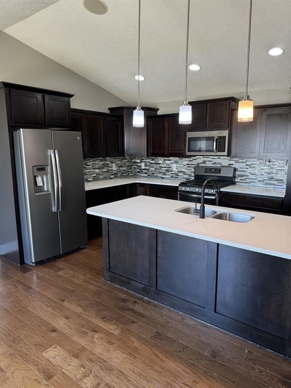 kitchen with dark brown cabinetry, tasteful backsplash, pendant lighting, vaulted ceiling, and appliances with stainless steel finishes