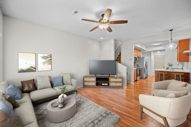 living room with ceiling fan, sink, and light hardwood / wood-style flooring