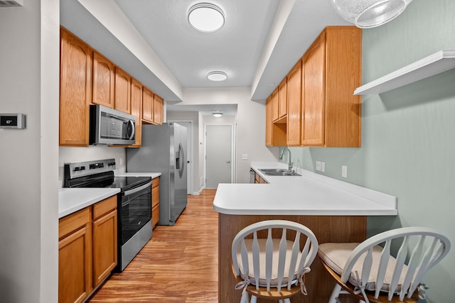 kitchen with a kitchen bar, sink, appliances with stainless steel finishes, kitchen peninsula, and light hardwood / wood-style floors