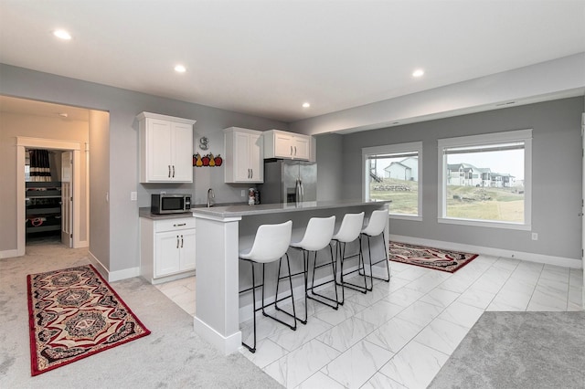 kitchen with white cabinets, appliances with stainless steel finishes, a kitchen island with sink, and a breakfast bar area