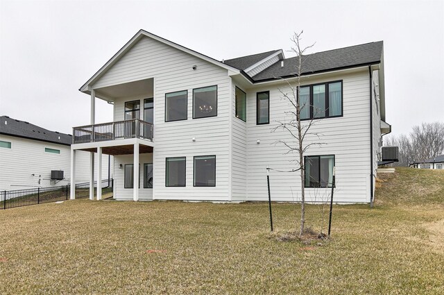 rear view of house with central air condition unit, a balcony, and a lawn