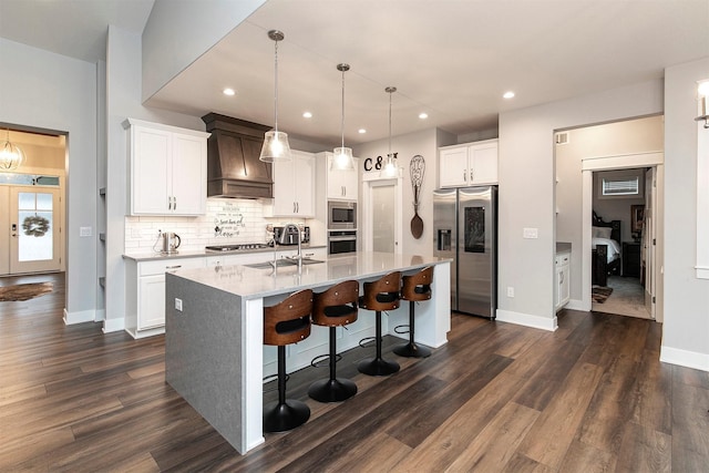 kitchen with stainless steel appliances, white cabinetry, a kitchen island with sink, and premium range hood