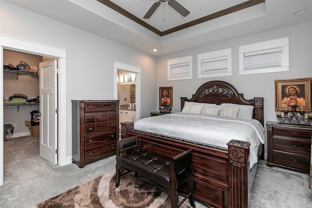 bedroom featuring ensuite bath, ceiling fan, a spacious closet, a tray ceiling, and light carpet