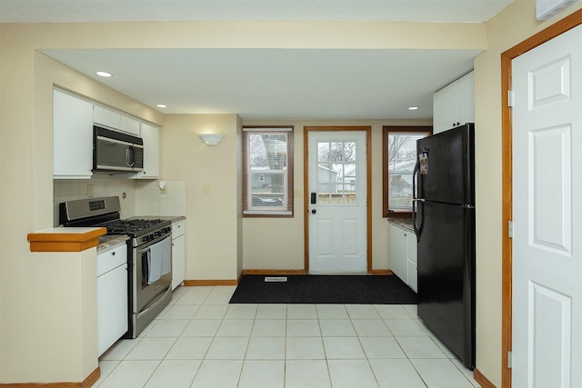 kitchen featuring black refrigerator, backsplash, white cabinetry, and stainless steel range with gas stovetop