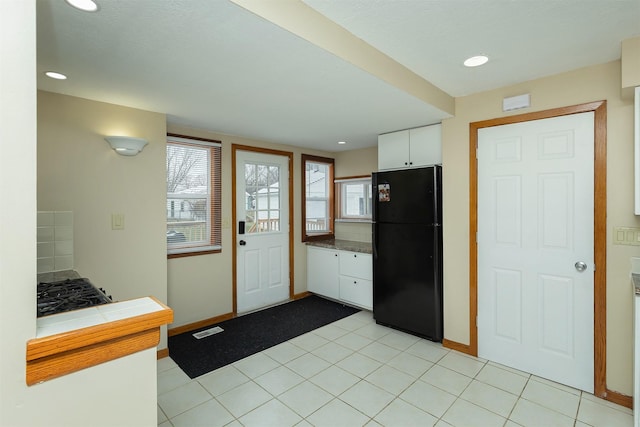 kitchen featuring black refrigerator, backsplash, white cabinets, and light tile patterned flooring