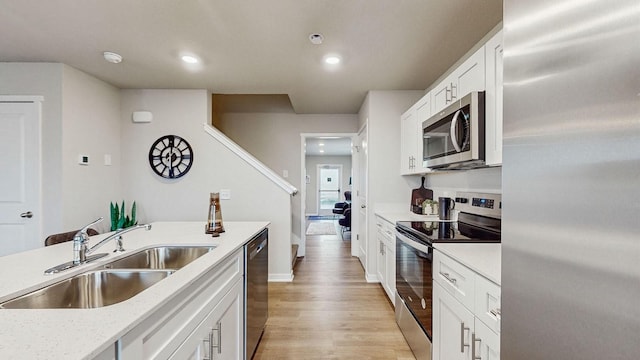 kitchen featuring white cabinetry, stainless steel appliances, sink, light stone counters, and light hardwood / wood-style flooring