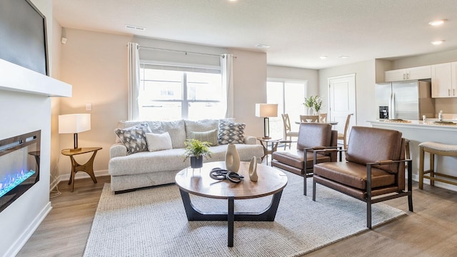 living room featuring recessed lighting, visible vents, baseboards, light wood-type flooring, and a glass covered fireplace