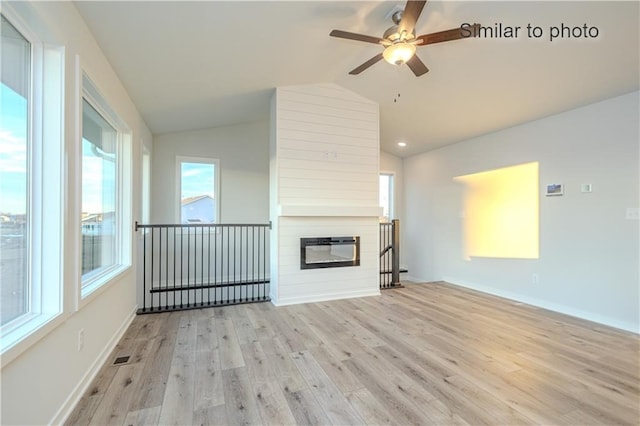 unfurnished living room with ceiling fan, a fireplace, vaulted ceiling, and light hardwood / wood-style flooring