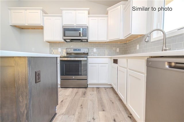 kitchen featuring tasteful backsplash, appliances with stainless steel finishes, light hardwood / wood-style floors, and white cabinets